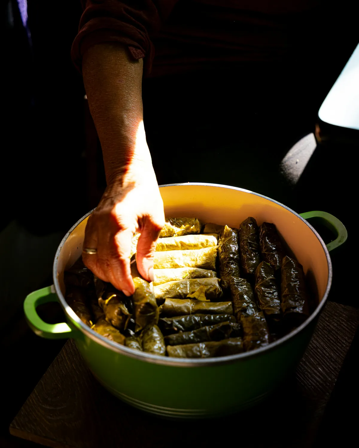 Hand layering stuffed grape leaves in a green pot