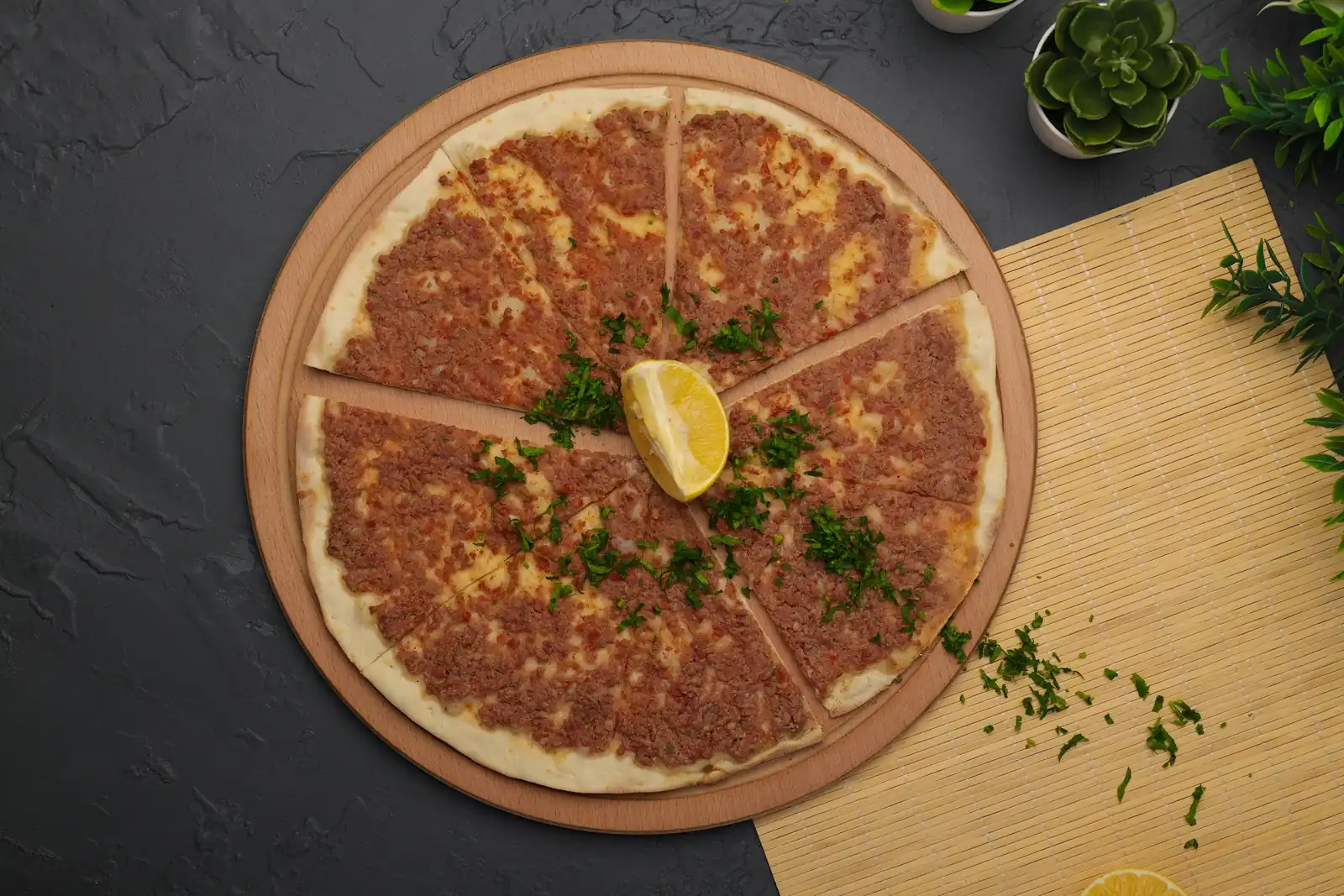 Sliced lahmacun with a lemon wedge and parsley on black stone