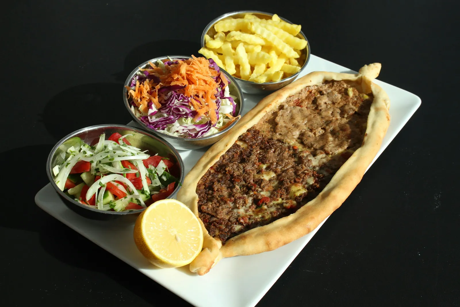 Ground meat pide with salad and fries on a white plate